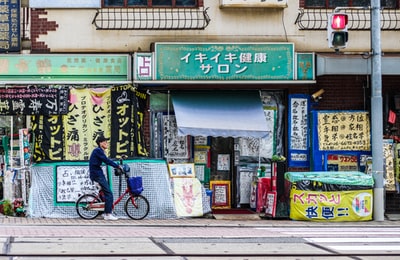 男子骑着红色折叠自行车停在蓝白店旁